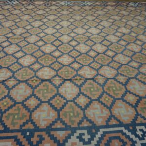 Flatweave rug with a large geometric pattern of navy blue diamonds and repeating peach, gray, and green symbols.