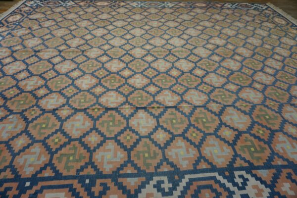 Flatweave rug with a large geometric pattern of navy blue diamonds and repeating peach, gray, and green symbols.