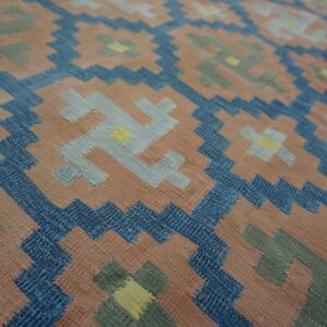 Geometric design flatweave rug with salmon, navy, sage, and light blue interlocking stepped motifs.