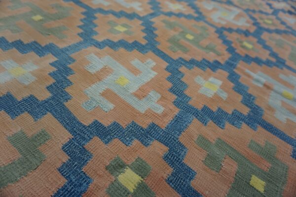 Geometric design flatweave rug with salmon, navy, sage, and light blue interlocking stepped motifs.