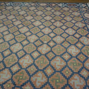 Geometric flatweave rug in peach, blue, and green on rustic wood flooring.