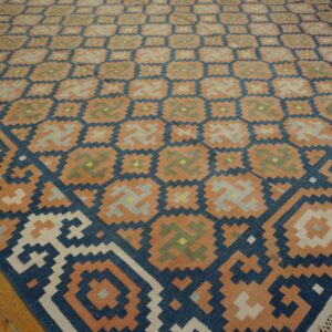 Terracotta and blue geometric flat-weave rug with fringe lays on a distressed hardwood floor.