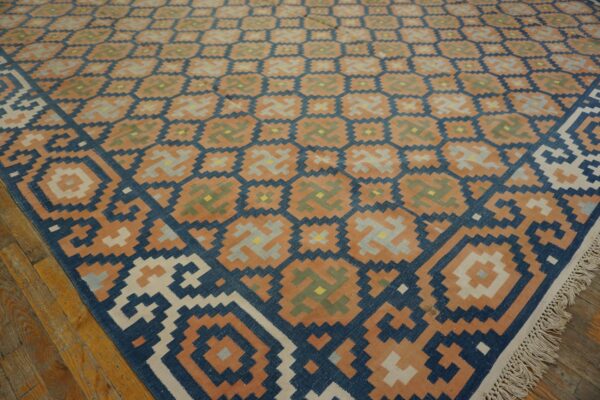 Terracotta and blue geometric flat-weave rug with fringe lays on a distressed hardwood floor.
