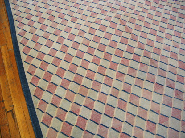 Flatweave rug features a rose, cream, and blue geometric cube pattern next to hardwood plank flooring.