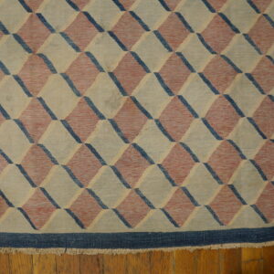 Beige, red, and blue flatweave rug with a tumbling block geometric pattern on wood flooring.