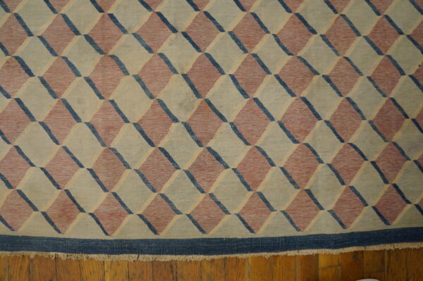 Beige, red, and blue flatweave rug with a tumbling block geometric pattern on wood flooring.