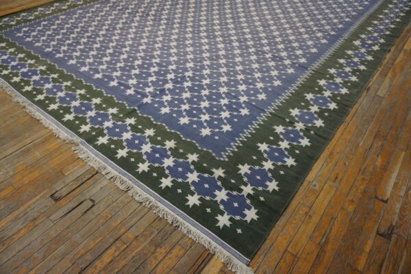 Large flat-woven rug featuring a blue, white, and dark green star pattern on distressed wooden planks.
