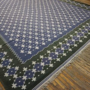 Low-pile rug with blue and white stars and a green border resting on distressed hardwood flooring.