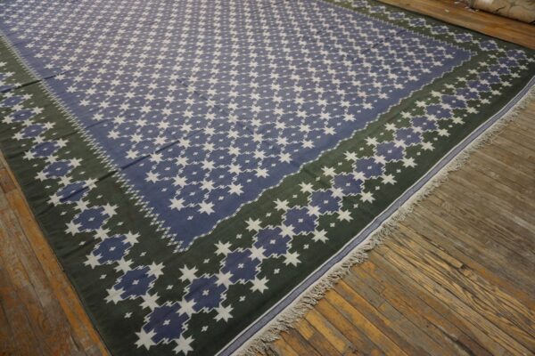 Low-pile rug with blue and white stars and a green border resting on distressed hardwood flooring.