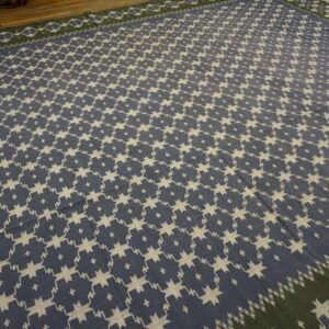 Geometric blue and cream flatweave rug covering a wooden floor, featuring a dark green border.