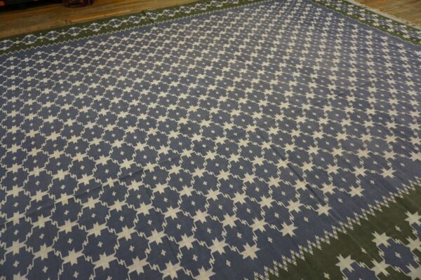 Geometric blue and cream flatweave rug covering a wooden floor, featuring a dark green border.