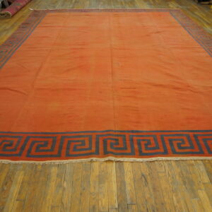 Flat-weave terracotta rug featuring a wide slate-blue geometric key border on worn wood plank flooring.
