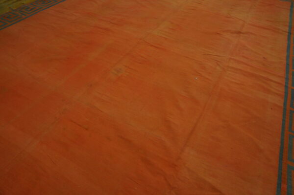 Rust-colored rug with strong color striations and a geometric blue-green border visible on two sides.