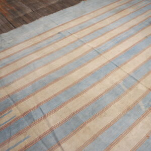 Faded blue and beige striped flatweave rug displayed on rustic wood plank flooring.