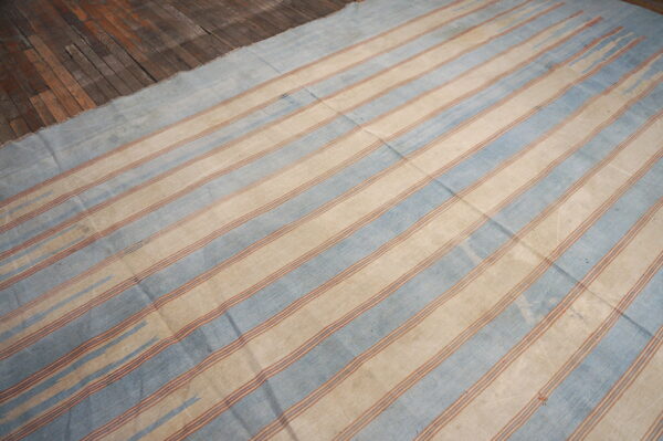Faded blue and beige striped flatweave rug displayed on rustic wood plank flooring.