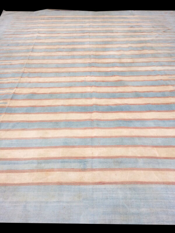 Low-pile rug with alternating pale blue and cream horizontal stripes featuring thin reddish lines.