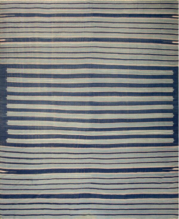 A large flat-weave rug with alternating wide bands of navy blue and off-white stripes lies on a wood floor.