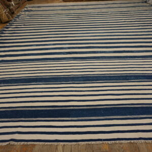 A large flat-weave rug with alternating wide bands of navy blue and off-white stripes lies on a wood floor.