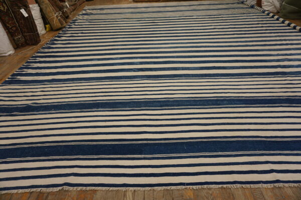 A large flat-weave rug with alternating wide bands of navy blue and off-white stripes lies on a wood floor.