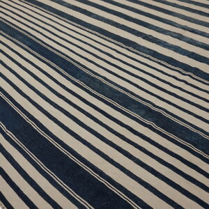 A low-pile rug features wide indigo and light beige vertical stripes with thin white accent lines.
