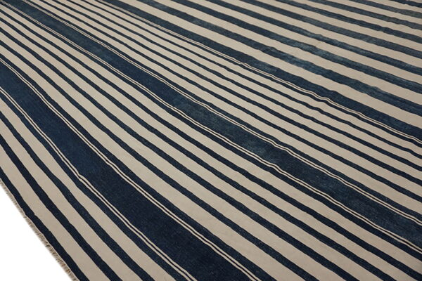 A low-pile rug features wide indigo and light beige vertical stripes with thin white accent lines.