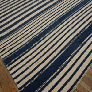 Navy blue and cream striped flatweave rug with visible fringe lying on rustic wooden flooring.