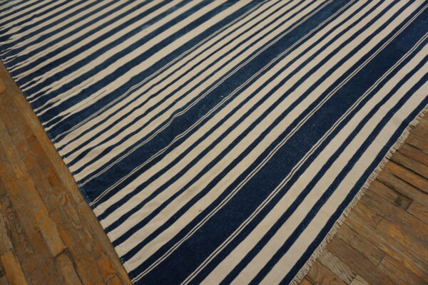 Navy blue and cream striped flatweave rug with visible fringe lying on rustic wooden flooring.