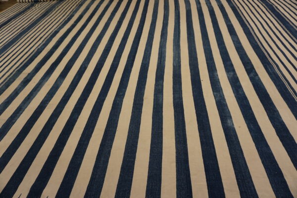 Textured rug featuring alternating wide vertical stripes of dark blue and cream color.