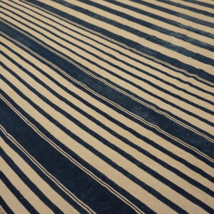 A low-pile rug featuring bold indigo and off-white stripes lies diagonally across a wooden plank floor.