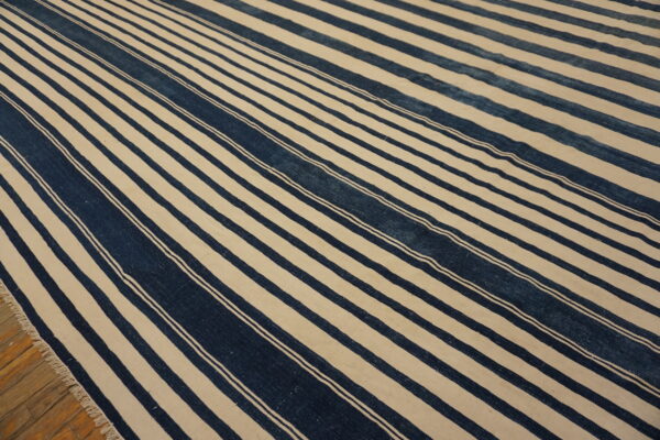 A low-pile rug featuring bold indigo and off-white stripes lies diagonally across a wooden plank floor.