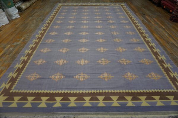 Blue rug with repeating orange lozenges and a thick geometric border of brown and pale yellow triangles.
