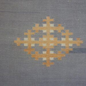 Flatweave rug detail showing a gray-blue field with an orange geometric center and brown and yellow diamond border.