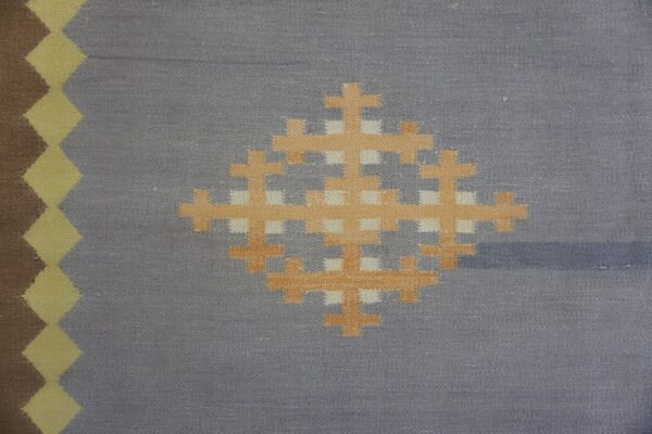 Flatweave rug detail showing a gray-blue field with an orange geometric center and brown and yellow diamond border.