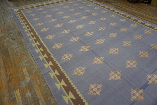 Blue-gray flatweave rug with yellow geometric patterns and brown borders rests on distressed wood flooring.