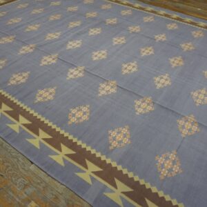 Flat-woven rug with gray-blue field, checkered diamonds, and a brown geometric border on wood floors.