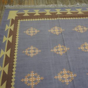 Flatwoven blue rug with a geometric yellow and brown border and repeating diamond motifs on a wood floor.