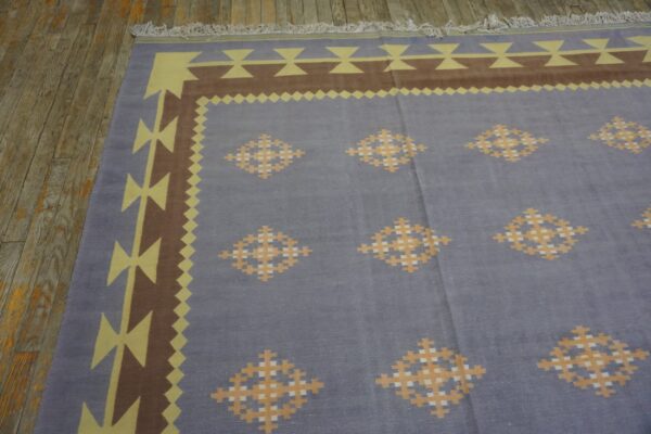 Flatwoven blue rug with a geometric yellow and brown border and repeating diamond motifs on a wood floor.