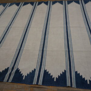 Off-white flatweave rug with vertical triple blue stripes and dark blue serrated zigzags on wood flooring.