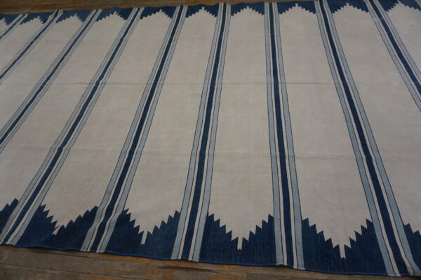 Off-white flatweave rug with vertical triple blue stripes and dark blue serrated zigzags on wood flooring.