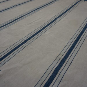 Flatweave rug with a light field, wide dark blue stripes, and serrated chevron end patterns.