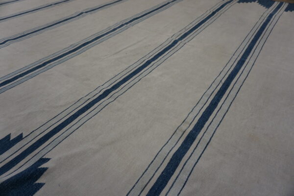 Flatweave rug with a light field, wide dark blue stripes, and serrated chevron end patterns.