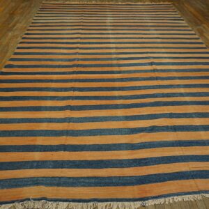 Low-pile rug featuring wide orange and dark blue horizontal stripes on rustic wood plank flooring.