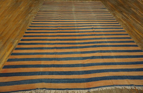 Low-pile rug featuring wide orange and dark blue horizontal stripes on rustic wood plank flooring.