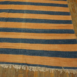 Flat woven rug featuring horizontal blue and tan stripes with fringe on rustic wooden floorboards.