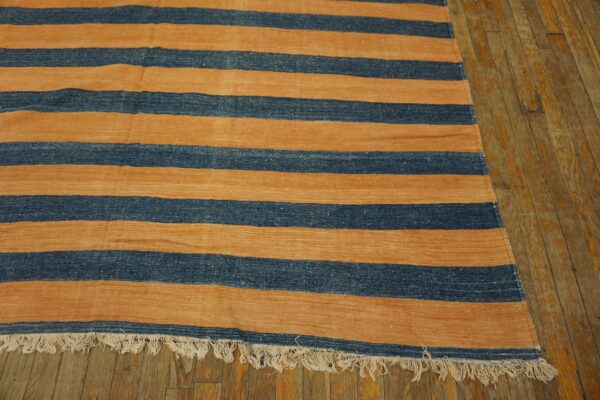 Flat woven rug featuring horizontal blue and tan stripes with fringe on rustic wooden floorboards.