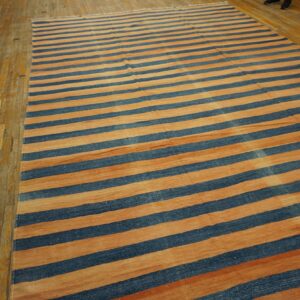 Large flatweave rug featuring wide alternating stripes of deep blue and warm terracotta on hardwood planks.