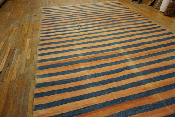 Large flatweave rug featuring wide alternating stripes of deep blue and warm terracotta on hardwood planks.