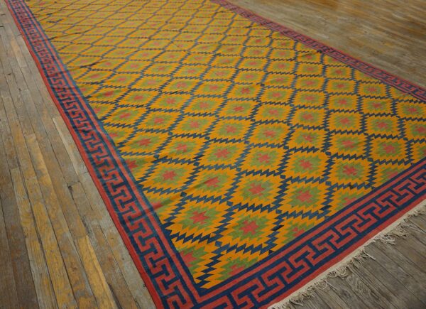 Flatweave rug in gold, navy, red, and green geometric diamonds with a greek key border on wood planks.