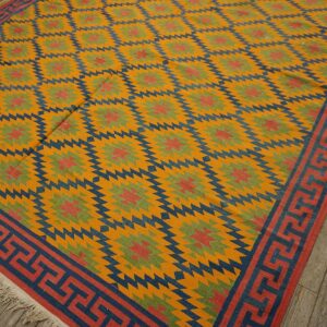 Geometric flatweave rug in yellow, blue, red, and green tones, featuring a Greek key border on wood flooring.