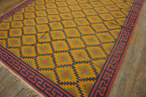 Geometric flatweave rug in yellow, blue, red, and green tones, featuring a greek key border on wood flooring.
